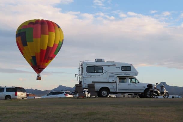 #069 - Grete StagebergLake Havasu City, Arizona1996 Ford F2502002 Bigfoot 25C8.11Camera Used - iPhone 7My husband and I both retired on the same day.  We hit the road in our truck camper four days later to explore Washington, Oregon, California, Nevada, Arizona, New Mexico, and Texas.  Our entire trip was 2½ months long and was our first, but definitely not our last, extended road trip in our camper.While on the road we learned of the Havasu Balloon Festival and Fair in Lake Havasu City, Arizona.  We made a reservation to dry camp at the festival site so that we could take in all the festivities.Our site was at an unused golf course that they had opened up to RV parking for the festival.  When we arrived, the area’s host was thrilled because she saw our truck camper.  She had a premier site for us since our rig was so small.  Much to our surprise and delight she directed us up to an old putting green up a small hill, where we had a commanding view of both the lake and the festival venue.As we were setting up our camp site, one of the neighboring Class A motorhome owners who had arrived before us came up and mentioned the host said they couldn't park on the green, and they were curious why we were able to.  Well, let’s just put it this way, the host said no large RVs on the green, just small rigs like ours.  Needless to say, we were especially thrilled to have a truck camper that weekend.The winds were rather unpredictable during the festival.  As hot air balloons floated overhead all around us we began running across the field toward our camper to watch the balloons dip and run on the lake.  What a surprise it was to get such a perfect cell phone photo while running across the field.